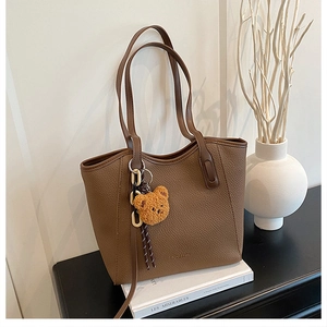 Brown lychee leather tote bag with a yellow bear charm on a minimalist desk