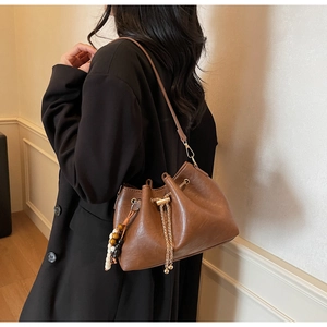 Detail of dark brown drawstring bucket bag with gold chain and beaded pendant