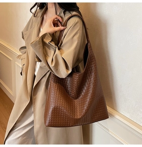 Close-up of a large brown woven hobo shoulder bag styled on a trench coat model