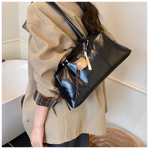 Detail of black glossy leather tote bag featuring baseball glove charm and white lettering