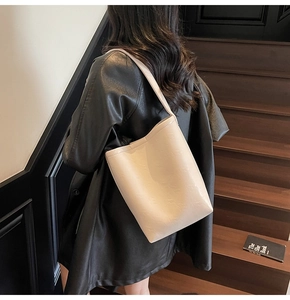 Sac fourre-tout minimaliste en cuir blanc crème posé sur un escalier en bois foncé