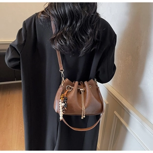Detail of dark brown leather bucket bag with drawstring closure and beaded chain accent