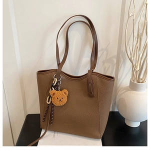 Detail of brown litchi pattern leather tote bag with golden logo and cute bear charm
