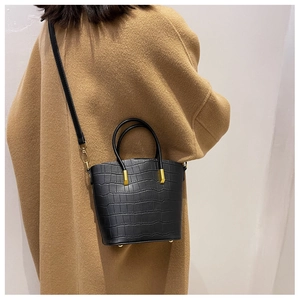 Detail of black crocodile texture handbag with gold metal accents on wool coat