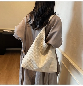Close-up of cream woven shoulder bag with wide strap on model in minimalist interior