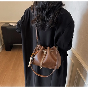 Brown leather bucket bag with drawstring and tassel detail shown as crossbody on model