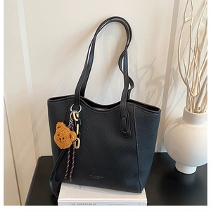Detail of black pebbled leather tote bag with gold logo, plush bear, and chain charms