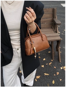 Detail of a brown leather Boston bag with decorative beaded charms on wooden bench