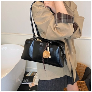 Detail view of black glossy shoulder bag with metallic letters and decorative woven charm