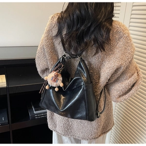 Detailed view of a black glossy leather backpack with a cute plush bear pendant accessory