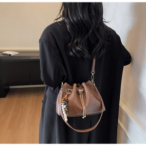 Detail of a brown pleated bucket bag with wooden bead charm and gold chain strap