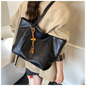 Dettaglio della borsa tote nera opaca minimalista con ciondolo vintage in legno e nappa