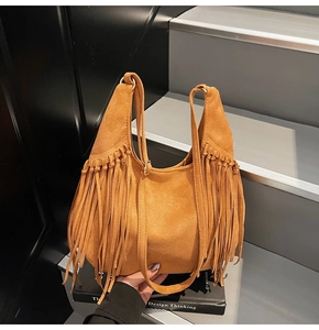 Detailed view of brown suede tote bag featuring bohemian fringes on a book background