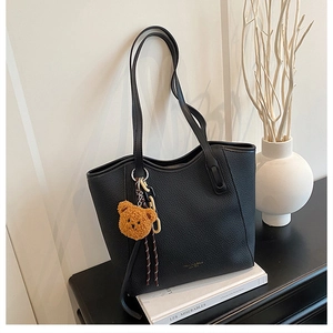Detail view of black pebble leather tote bag with gold logo and plush bear charm