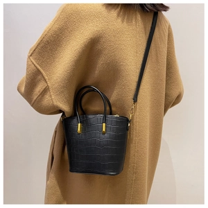 Detail of black crocodile texture bucket bag with gold hardware and a round handle