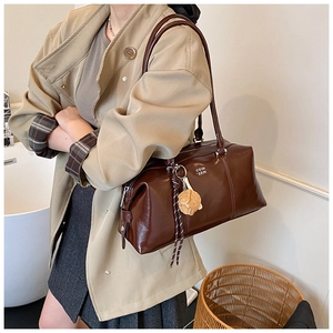 Detail of a dark brown glossy leather underarm bag with white logo and decorative charms