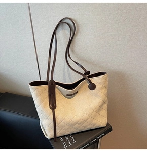Detail view of beige quilted tote bag with brown leather handles on a leather sofa