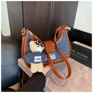 Detail of blue denim and brown leather crescent bag with cute teddy bear charm