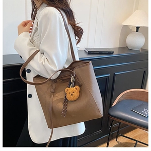 Brown lychee leather tote bag with cute plush bear pendant shown in a minimal home setting