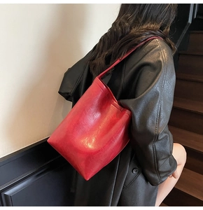 Détail du sac seau rouge vif en cuir porté à l'épaule avec une texture lisse et chic