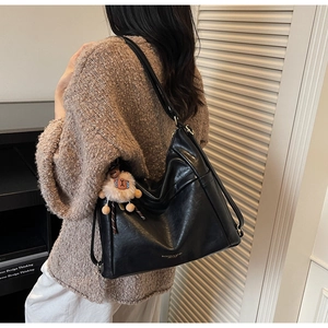 Detail of a black leather hobo bag with a soft white pompom charm on a leather strap