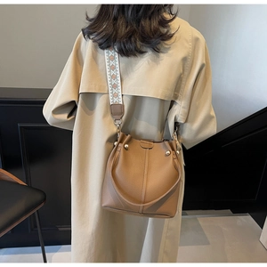 Détail du sac seau en cuir marron avec bandoulière brodée et rivets en métal doré