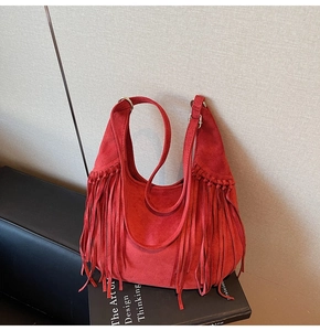 Close-up of a red suede hobo bag with long tassels and metallic rings in a studio setting