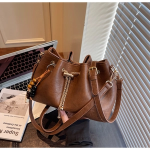 Detailed close-up of brown drawstring bucket bag with golden chain and wood bead charm