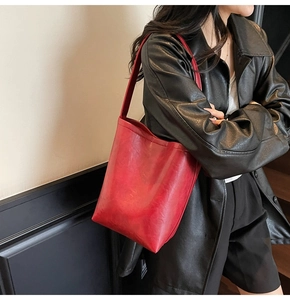 Close-up of a red oil-wax leather tote bag worn by a model in a modern indoor setting