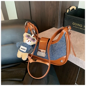 Detail of blue denim and brown leather crescent bag with bear charm and buckle