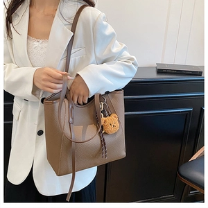 Detail of brown litchi leather tote bag with MAOMAO BAG logo and cute bear charm