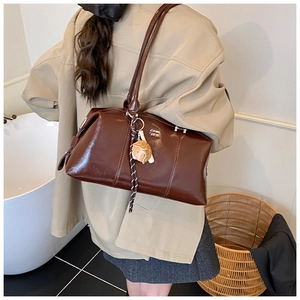 Detailed side view of a brown glossy leather underarm bag with decorative doll charm
