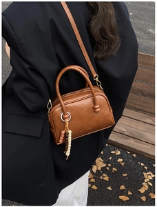 Détail du sac bowling en cuir marron avec breloque en perles et logo gravé en décor d'automne