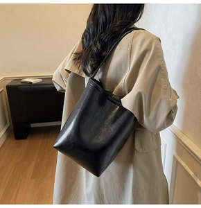Détail d'un sac seau noir minimaliste porté avec un trench-coat beige très élégant