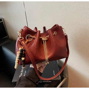 Detail of burgundy bucket bag with gold chain strap and decorative wood bead charm