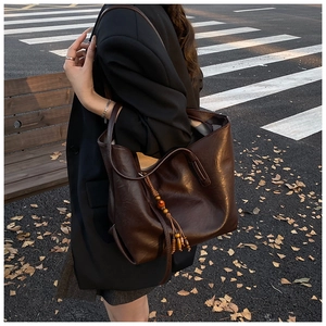 Dettaglio borsa shopper marrone scuro con nappa in legno in una strada autunnale