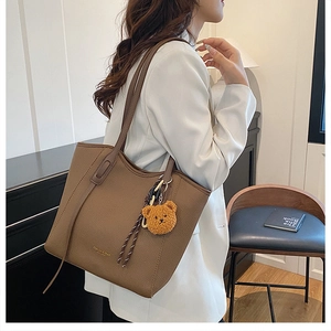 Detail of a large brown pebble grain tote bag with a cute plush bear charm on a strap