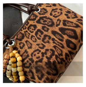 Detail of leopard print tote bag with brown leather handles and wooden bead charm