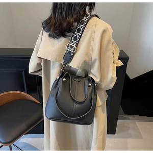Détail du sac seau noir en cuir avec bandoulière géométrique et rivets métalliques