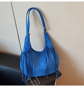 Close-up of a blue suede hobo bag featuring long bohemian tassels and adjustable gold buckle