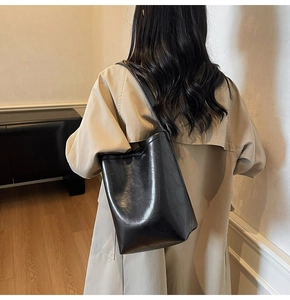 Détail d'un grand sac seau noir en cuir brillant porté avec un trench-coat beige élégant
