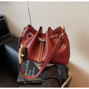 Close-up of burgundy pleated bucket bag with gold chain drawstring and beaded charm