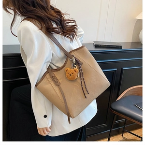 Detail of khaki lychee grain leather tote bag with plush bear charm worn with white blazer
