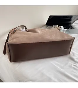 Détail d'un cabas en daim marron avec finitions cuir et breloque dans un cadre de vie