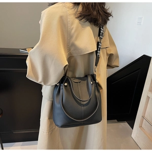 Détail du sac seau noir en cuir avec une bandoulière large aux motifs géométriques
