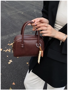 Detail of dark brown pebble leather bowling bag with bohemian beaded charm and gold text