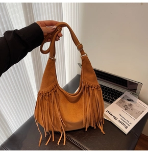 Detail of a brown faux suede crescent bag with long fringe accents and adjustable strap