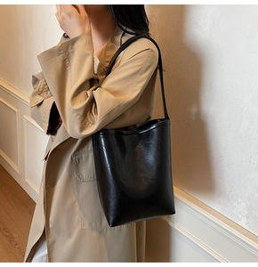 Close-up of a black glossy leather shoulder bucket bag shown on a model in a minimalist room