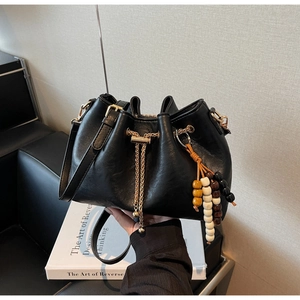 Close-up of black pleated bucket bag with gold chain drawstring and beaded charm