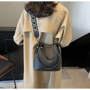 Détail du sac seau en cuir noir avec bandoulière géométrique porté à l'épaule